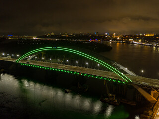 Obraz premium Aerial drone view. Modern arch cable-stayed bridge in Kiev in the evening. Colored lighting of the arch of the bridge.
