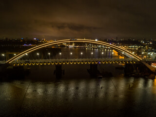 Aerial drone view. Modern arch cable-stayed bridge in Kiev in the evening. Colored lighting of the arch of the bridge.