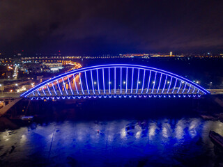 Obraz na płótnie Canvas Aerial drone view. Modern arch cable-stayed bridge in Kiev in the evening. Colored lighting of the arch of the bridge.