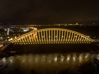 Naklejka na ściany i meble Aerial drone view. Modern arch cable-stayed bridge in Kiev in the evening. Colored lighting of the arch of the bridge.