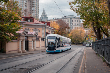 Obraz premium A modern tram runs along Dostoevsky Lane. Historical center of Moscow. On the right is an old wooden fence. On the left is an old building. In the background are modern buildings. Fall.