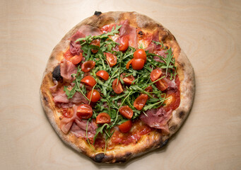 Italian pizza topped with tomato sauce, mozzarella, prosciutto, rocket salad and cherry tomatoes, top view on wooden background
