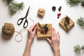 Christmas composition. Female hands keeping christmas gifts, pine branches, toys on white background. Flat lay, top view, copy space.