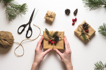 Christmas composition. Female hands keeping christmas gifts, pine branches, toys on white background. Flat lay, top view, copy space.