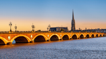 Fototapeta premium Bordeaux, France. Panoramic view of Pont de Pierre, old stone bridge over the river Garonne, and Saint Michel cathedral at sunset.