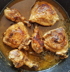 Chicken legs stewed with garlic and thyme. Dish is in black frying pan on the white gas stove