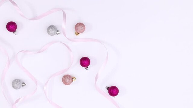 Pastel pink and silver Christmas ornaments and ribbons appear on white theme. Stop motion