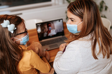 Middle age doctor talking and examining little girl using laptop computer and internet connection. They are chatting while doctor gives health advices. Telehealth concept.