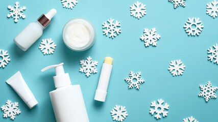 Winter cosmetic products set on blue background. Lipstick, cream jar, pump bottle, tube package mockup and snowflakes. Flat lay, top view.