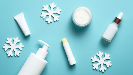 Set of cosmetic products and snowflakes on pastel blue background. Winter skin care concept. Pump bottle, lipstick, cream jar, serum. Flat lay, top view
