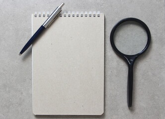 A spring notebook with a sheet of craft paper A5 with a ballpoint pen and black magnifying glass on...