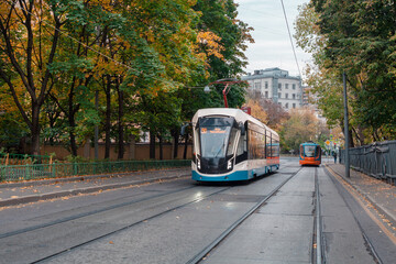 Obraz premium Two modern trams driving along Dostoevsky Lane in different directions. Historical center of Moscow. On the right is an old wooden fence. Fall. Translation: Metro Novoslobodskaya. Stop. 