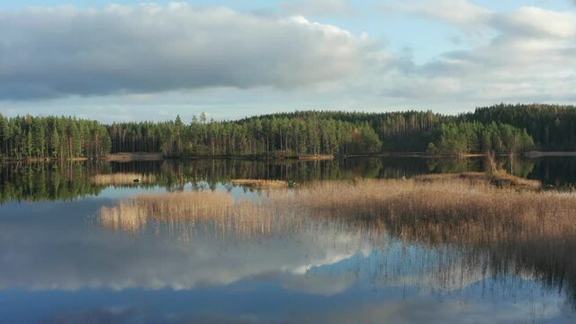 Swedish remote wilderness. Drone shot over lake and forest. Calm sunny day with clouds and sky mirror like on reflecting water surface. Low flying aerial nature view in sweden