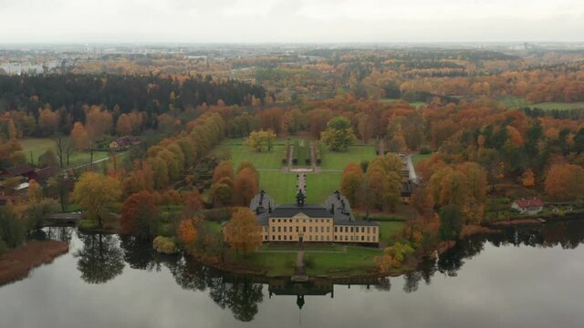 Swedish castle on cloudy day in autumn fall. Aerial drone shot of royal park in Sweden Stockholm. Ulriksdal palace and colorful park in fall. Edsviken lake calm surface mirroring building