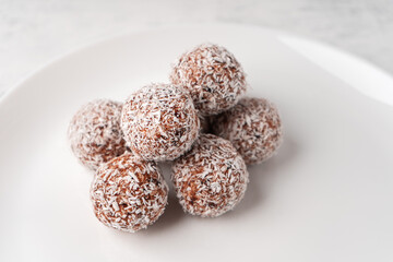 Candy balls made of dates and coconut shavings in a white dish on a light background