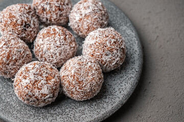 Fototapeta na wymiar Round vegetarian sweets made of dates and coconut shavings lie on a gray concrete plate on a gray concrete table close-up
