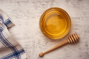 Fresh acacia honey in a glass bowl near a wooden honey spoon and towel, top view