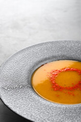 Pumpkin soup sprinkled with paprika in a gray plate with large margins close-up