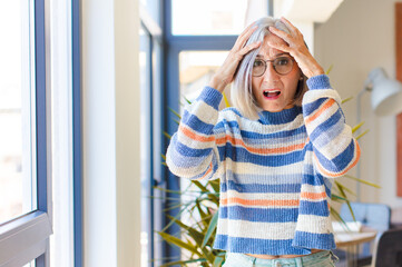 middle age woman feeling horrified and shocked, raising hands to head and panicking at a mistake