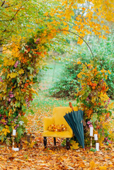 Wedding arch decorated with leaves and flowers, soft yellow armchair and umbrella on the background...
