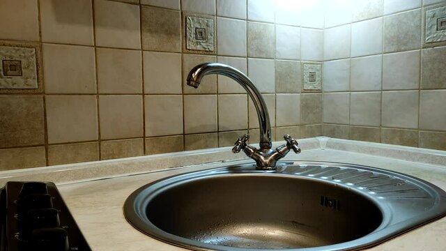 A man closes a tap in the kitchen from which water is dripping. Leaking faucet in the kitchen sink.
