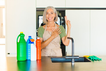 middle age woman looking happy, confident and trustworthy, smiling and showing victory sign, with a...