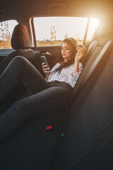 Obraz premium Young woman lying on backseat of car using smartphone