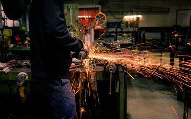Man worker uses grinder on piece of metal making sparks. Metal processing, metal cutting and finishing. Metal industry