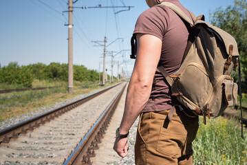 Man with a backpack on his back is waiting for a train at the railroad station platform.