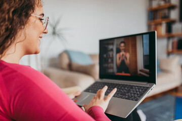 Young adult overweight girl exercising at home watching an instructor via laptop computer. Online fitness and pilates workout.