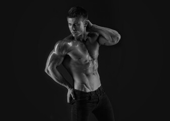 Naklejka na ściany i meble Muscular model sports young man on dark background. Fashion portrait of strong brutal guy. Sexy torso. Male flexing his muscles. Black and white photo.
