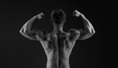 Model sports young man on dark background. Sporty muscle guy showing his back and 
big shoulders. Sexy male flexing his muscles. Black and white photo.