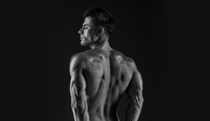 Model sports young man on dark background. Sporty muscle guy showing his back and 
big shoulders. Sexy male flexing his muscles. Black and white photo.