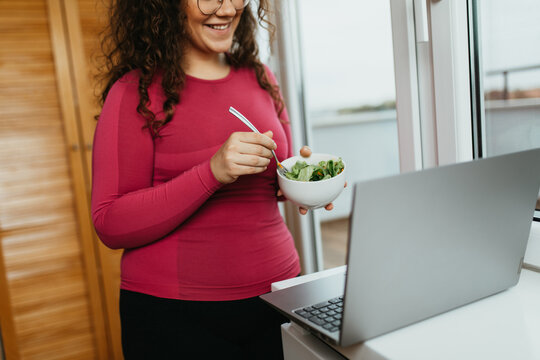 Young Adult Overweight Woman Practicing Healthy Eating Diet At Her Home. She Uses Laptop Computer For Watching Diet Tutorial.