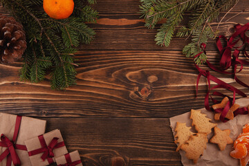 Top view of Christmas gingerbread cookies, presents, tangerins and branches of Christmas tree on dark wooden background.
