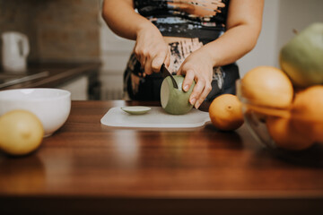 Young overweight woman slicing fresh fruit and preparing healthy meal in home kitchen.