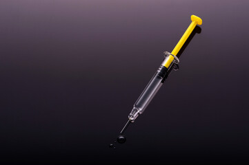 Yellow Syringe on glossy black background.  Dark side of Immunization, vaccination, or drugs and darkness conmcept.