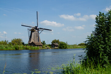 Fototapeta premium Kinderdijk, The Netherlands, August 2019. On a beautiful summer day a historic windmill, in perfect condition, in the Dutch countryside furrowed by canals lined with tall green grasses.