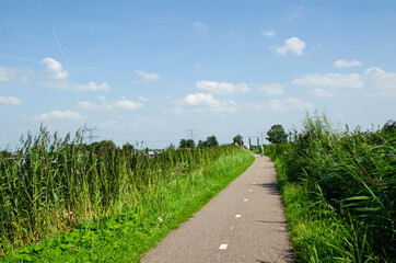 Kinderdijk, The Netherlands, August 2019. A small road winds through the Dutch countryside, lined with very green grass. Beautiful sunny day, in the distance you can see a cyclist.