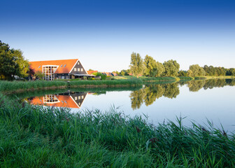 Obraz premium Kinderdijk, The Netherlands, August 2019. Amazing Northern European landscape: the evening light enhances the colors and the reflection of the house and the trees in the water mirror.