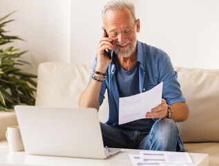 Cheerful aged freelancer making call in home office.