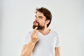 Emotional bearded man in a white t-shirt gestures with his hands light background