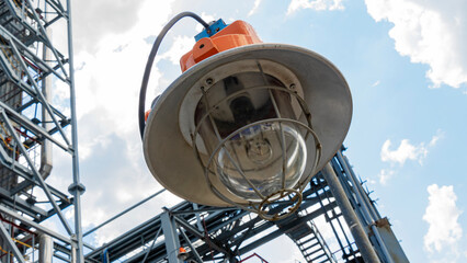 Industrial explosion proof lantern on the background of the refinery plant and classic blue sky with clouds. Space for text.