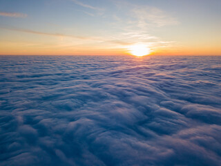 Sunset over curly clouds, aerial high flight. The last rays of the sun shine on the clouds.