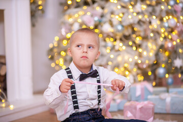 Christmas tree, a boy with Down syndrome sits on the floor and holds a box with a gift in his...