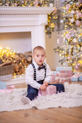 Christmas tree, a boy with Down syndrome sits on the floor and holds a box with a gift in his...