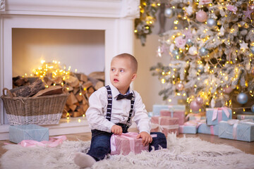 Christmas tree, a boy with Down syndrome sits on the floor and holds a box with a gift in his...