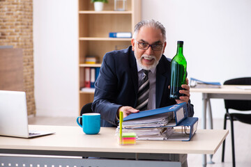 Old male employee drinking alcohol in the office