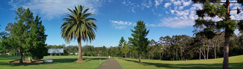 Fototapeta na wymiar Beautiful panoramic view of a park with green grass and tall trees and deep blue sky with light clouds in the background, Heritage park, Castle Hill, Sydney, New South Wales, Australia 