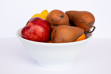 Pears of the Kaiser Alexander variety , apple, orange and other fruits in a white bowl on a wooden table and white background